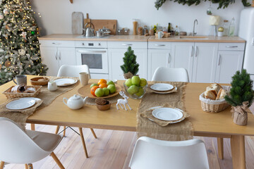 There is a Christmas tree in the corner by the kitchen window. A set festive table for the whole family.
