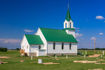 Fototapeta premium A small white church with a green roof sits in a field