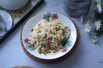 A plate of fried rice garnished with fresh green vegetables and anchovies, served on a floral-patterned plate.  Famously known in Malaysia as Nasi Goreng Kampung.
