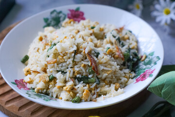 A plate of fried rice garnished with fresh green vegetables and anchovies, served on a floral-patterned plate.  Famously known in Malaysia as Nasi Goreng Kampung.