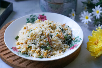 A plate of fried rice garnished with fresh green vegetables and anchovies, served on a floral-patterned plate.  Famously known in Malaysia as Nasi Goreng Kampung.