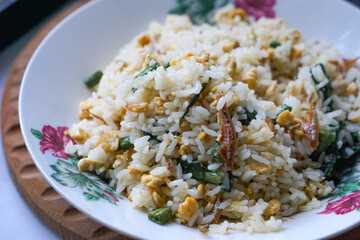 A plate of fried rice garnished with fresh green vegetables and anchovies, served on a floral-patterned plate.  Famously known in Malaysia as Nasi Goreng Kampung.