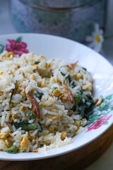 A plate of fried rice garnished with fresh green vegetables and anchovies, served on a floral-patterned plate.  Famously known in Malaysia as Nasi Goreng Kampung.