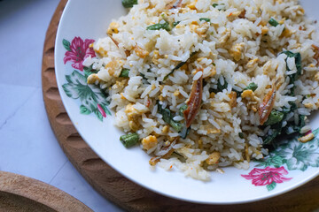 A plate of fried rice garnished with fresh green vegetables and anchovies, served on a floral-patterned plate.  Famously known in Malaysia as Nasi Goreng Kampung.