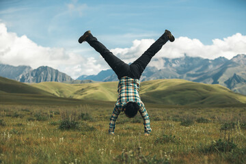 Woman hiker doing a handstand on high altitude mountain top grassland