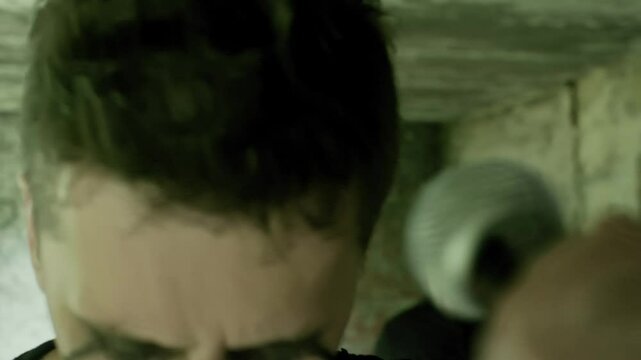 Lead vocalist singing with passion into Shure microphone with dark makeup and bandmate playing drums in abandoned building, creating powerful music performance