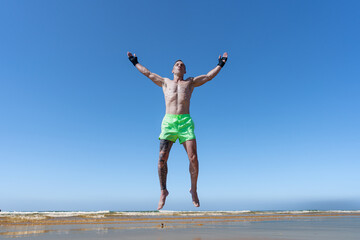 Obraz premium Hombre luchador de ckic boxing muy a gusto recargándose con la energía del sol, el mar y el contacto con la naturaleza un sensacional díe de verano en vacaciones soleado y con cielo azul.