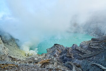 Sulphuric acid lake at Ijen volcano in Indonesia surrounded by misty mountains and fumaroles