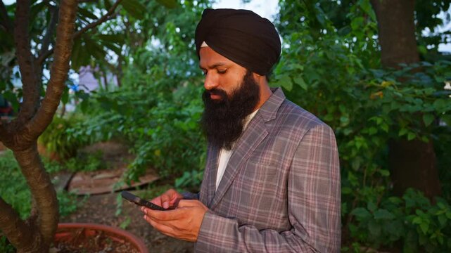 Turban man standing outdoor typing message on phone