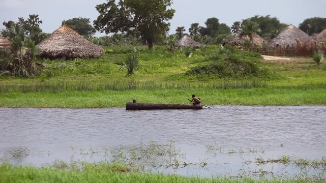 Village along the Nile River in South Sudan with people in dugout canoe.