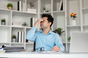 Stressed Office Worker Experiencing Headache from Overwork in Modern Workspace with Laptop and Documents