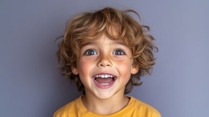 Happy toddler boy with curly hair and big smile against gray background.