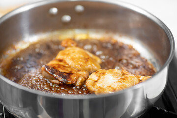 Sizzling chicken thighs cooking in a pan with rich sauce on stove