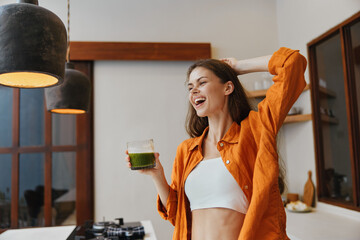 Happy young woman enjoying healthy green smoothie in stylish kitchen, radiating positive energy and wellness vibes during morning routine