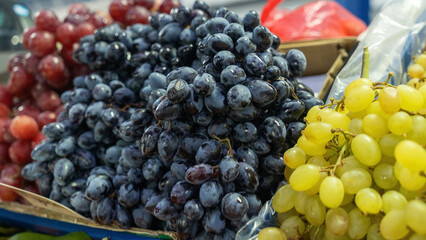 A close-up of a luscious black grape bunch displayed at a vibrant market. The rich, dark color and plump texture of the grapes invite shoppers.