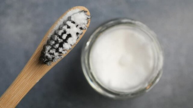 A wooden bowl of baking soda, a bamboo toothbrush, and a glass jar on a fabric