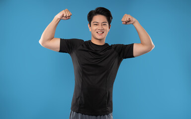 Portrait of young Asian man wearing gym clothes posing on blue background