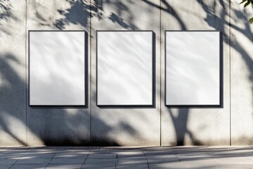 Three blank posters on a concrete wall with tree shadows.