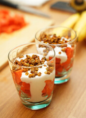 Two glasses of vegetarian yogurt dessert with papaya and granola on a wooden table