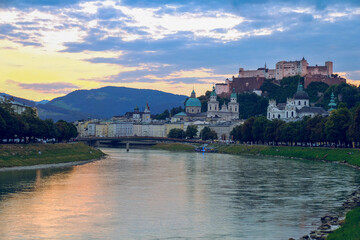 Obraz premium The city of Salzburg with historical buildings bisected by a winding Salzach River and mountain ranges in the background