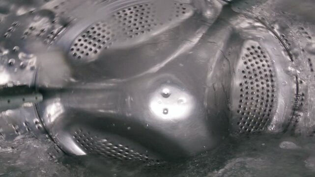 Close-up of a rotating drum of a washing machine filled with water. View from inside the washing machine
