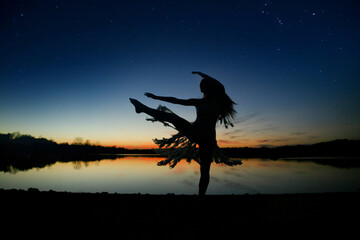 Silhouette of a dancer by a serene lake at sunset under starry sky