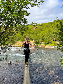 Woman balances on log over clear stream
