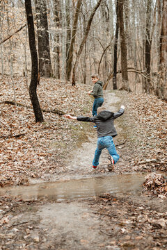 Boys jumping over stream on winter hike