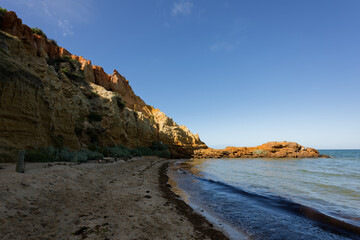 Rocky outcrop illuminated by the sun at Melbourne's Red Bluff, with beach and sandstone cliffs in shadow, early in the morning