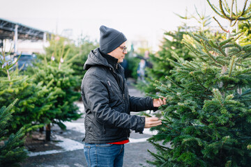 Man selecting a Christmas tree at an outdoor market on a cold day.