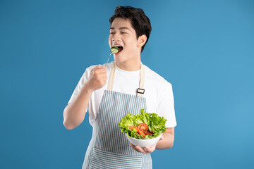 Portrait of a young Asian chef holding a bowl of salad and posing against a blue background