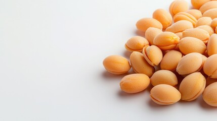 A close-up of a pile of light orange, oval-shaped seeds on a clean, white surface, showcasing their smooth texture and natural hue.