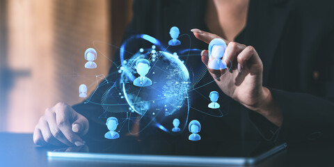 Businesswoman interacting with a digital network of human icons over a tablet.