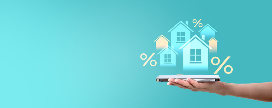 Hand holding smartphone with house icons and percent symbols on turquoise background.