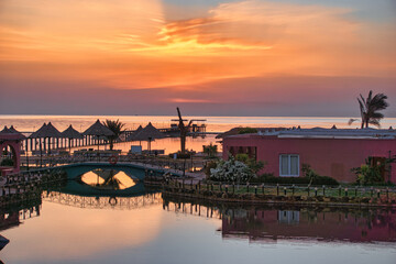 Obraz premium Fantastic sunrise in Marsa Alam over the Red Sea. visible palm trees, beach umbrellas, typical hotel buildings. Egypt, Marsa Alam 2024