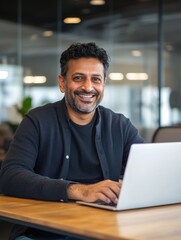 Fototapeta premium Happy smiling ethnical indian businessman having online virtual meeting call on laptop looking at screen sitting at table in coworking creative office, professional manager talking to employees.