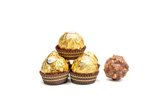 A stack of Ferrero Rocher chocolates with one chocolate on top. Golden colored candies with a chocolate center.