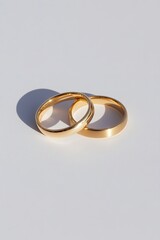 pair of gold wedding bands intertwined and placed on pristine white background with elegant shadows