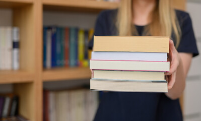 Dziewczyna w bibliotece, trzyma w dłoniach stos książek, wiedza i edukacja koncept