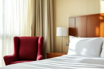 Modern hotel room with burgundy armchair and warm sunlight illuminating light gray linens and wooden furnishings