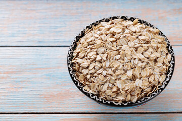 Bowl of Uncooked Oat Flakes Placed on Rustic Wooden Surface, Top View, Copy Space