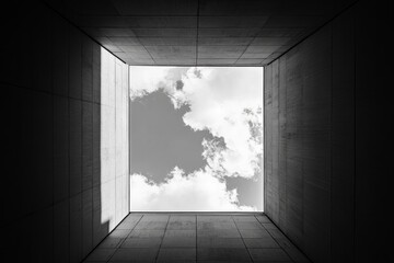 View of cloudy sky from inside concrete building with square opening