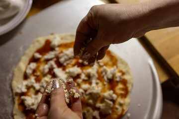 Hands Sprinkling Cheese on Homemade Pizza with Tomato Sauce