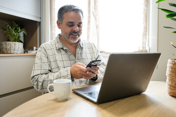 Man using smartphone and laptop at home office desk