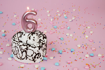 Birthday cake with burning candle number 6 and many sprinkles on pink background. Copy space for text.