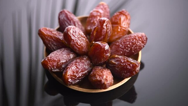 Dates fruit. Medjool Date fruits with palm tree leaf reflections on black background. Heap of dates rotating in a wooden bowl close up. Tasty healthy food. 