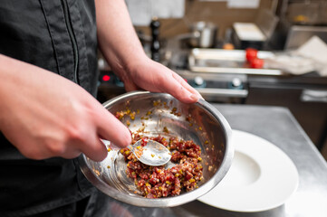 A chef prepares a dish by mixing ingredients in a stainless steel bowl. The kitchen is well-equipped, showcasing a professional cooking environment with various tools and utensils.