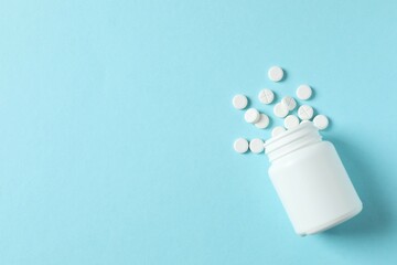 White pills pouring out of medicine bottle on color background