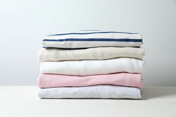 Stack of perfectly folded clothing items. Pile of different pastel color shirts, sweaters and other garments on white background. Close up, copy space