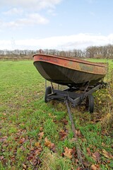 A neglected steel rowing boat on a trailer on the edge of a meadow.